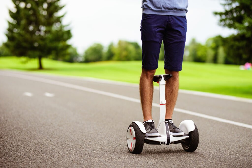 Close up of a man driving through the park on a knee-bar hoverboard.