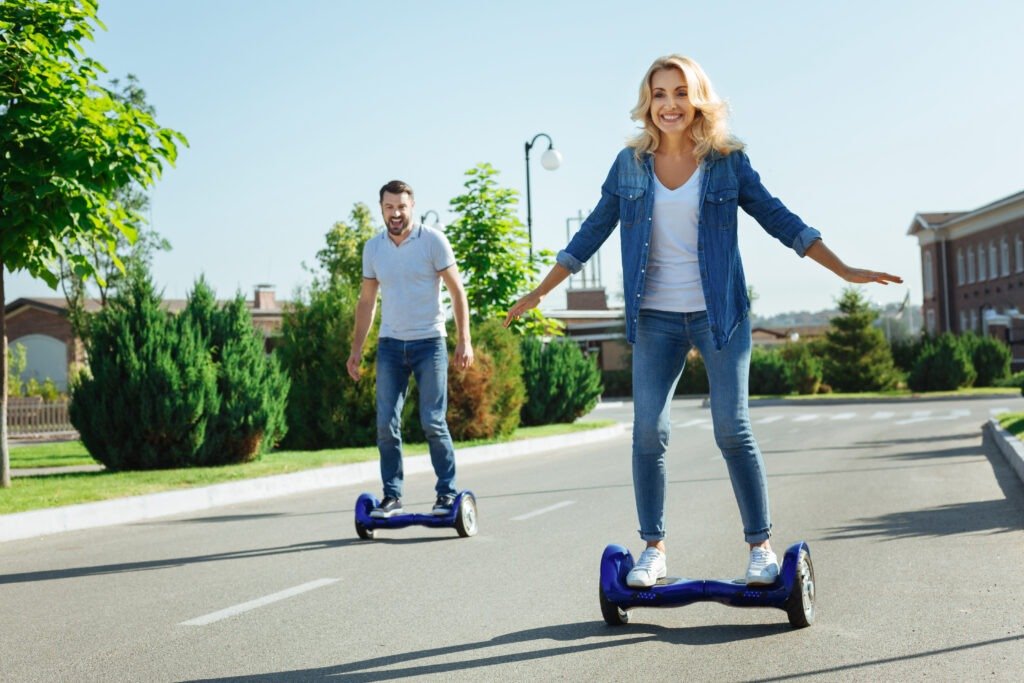 Happy couple riding self-balancing scooters on asphalt