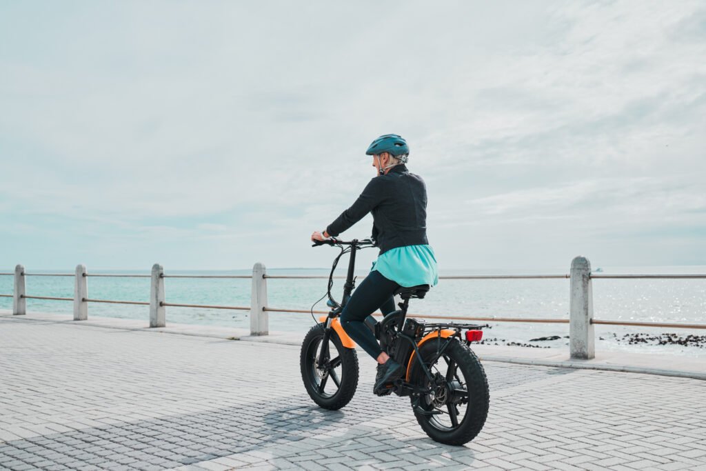 mature woman riding an electrical bike by sea side mature woman wearing a helmet and riding an electrical bike by sea side